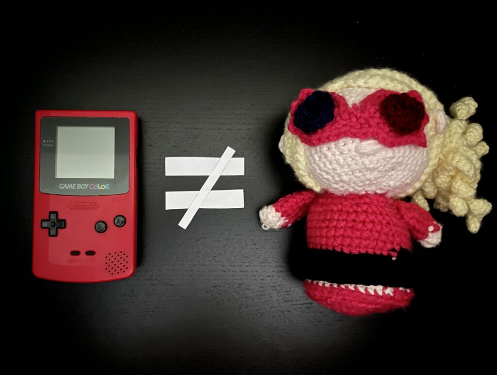 Links liegt ein Game Boy, rechts eine menschlich aussehende Häkelpuppe. Dazwischen ein Ungleichheits-Zeichen.